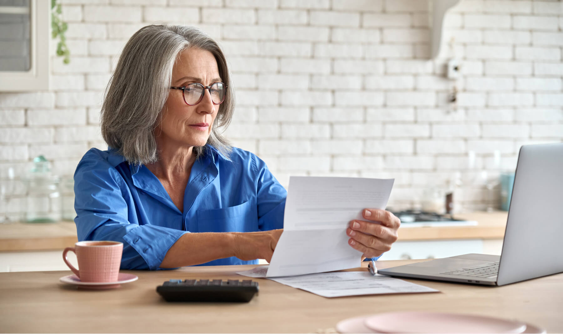 middle aged woman at table holding document calculating bank loan payments